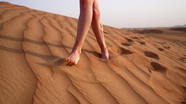 Close-up beautiful female legs in shorts walking on desert sand. Enjoying traveling and relaxing in fresh air in dunes under scorching sun in heat. Summer holidays in another country on vacation.