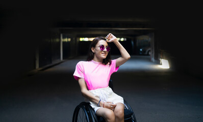 Fototapeta na wymiar Happy smiling young adult woman with sunglasses in a wheelchair dancing