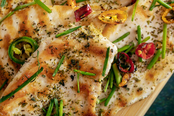 Macro close-up of grilled chicken breast cooked with three different colors chili peppers and aromatic herbs.