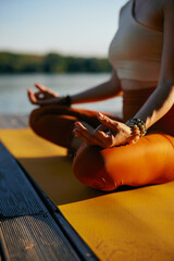 Cropped picture of a woman sitting on a dock near water in a lotus yoga pose and meditating.