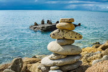 Fototapeta na wymiar Smooth stones stacked on each other on the beach. Tower of stones for meditation on a sea against blue sea background. Concept of balance and zen