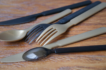 gold and black plastic cutlery, set of knives, spoons, forks on a wooden surface