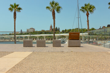 stone and wood seats looking at the Malaga marina with green palm trees, yachts and cathedral in the background