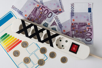 Power strip with several sockets with some of them blocked, surrounded by bills and coins. Concept of energy saving or restriction and responsible use of electricity
