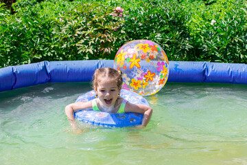 Cheerful caucasian girl swimming in pool with inflatable ring and ball outdoor, child playing in backyard, horizontal photo