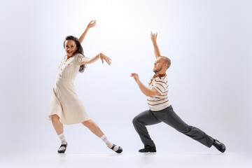 Fototapeta na wymiar Excited young man and woman in retro style outfits dancing lindy hop isolated on white background. Timeless traditions, 60s ,70s american fashion style.