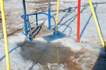 Multi-colored metal and wooden swing on the snow-covered playground