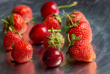A view of several varieties of fruit and berries scattered on a silver surface, featuring strawberry and cherry.