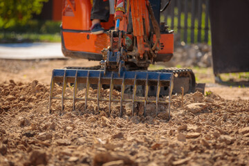 Obraz premium A mini excavator with a rake loosens the ground. landscape preparation