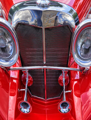 Radiator grille of red vintage car with horns of horn and big headlights on the side