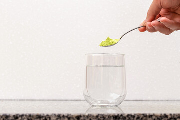 Green powder in a spoon (matcha tea) over a clear glass.