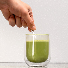 green Matcha tea in a glass, above it a hand with a spoon stirs it