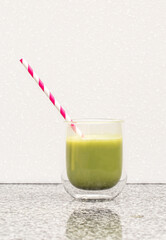 Matcha tea in a glass cup with a red straw stands on a steel 