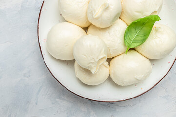 Cheese collection, white balls of soft Italian cheese mozzarella, served with fresh basil leaves on a light background, place for text, top view