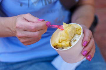 A girl in a blue t-shirt eats popsicles from a paper cup.