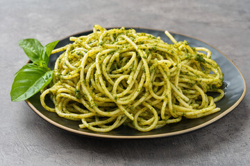 Plate of spaghetti with pesto sauce on gray stone background.