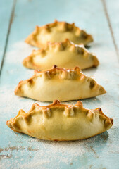 Row in perspective of four fresh baked empanadas, on a blue wooden table, afternoon lighting