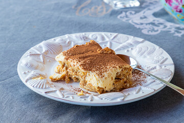 Tiramisu cake in a white plate on the table with a spoon.