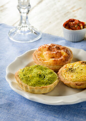 Three delicious quiches of different flavors on a ceramic plate, on a blue placemat, with wood table set