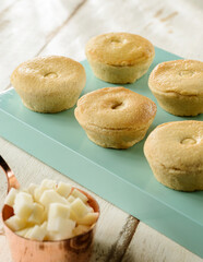 Six freshly baked brazilian empadas or patty on a green board, with palm heart pieces on foreground and wood table background