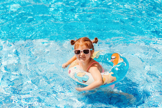 Cute toddler girl wear sunglasses having fun in swimming pool with blue clean water. Family vacation in luxury resort.