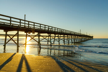 Sunrise behind a fishing pier at dawn on the Atlantic Ocean in Sunset Beach, North Carolina.