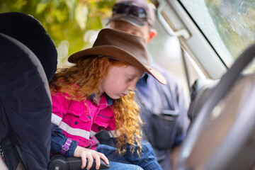little girl wearing hi-vis in car seat with her father in background