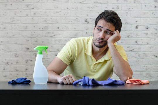 Tired handsome man in yellow t-shirt sits at the table and feeling bad after exhausting cleaning day. Household concept