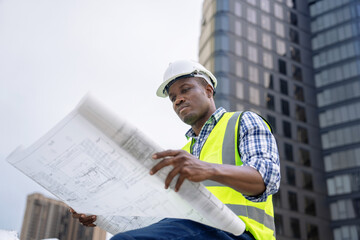 African male civil engineer inspects a commercial building construction site in a real estate...