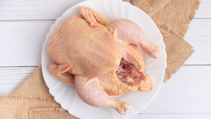 Whole raw organic chicken on a plate on white wooden background, selective focus. Healthy food, diet, or cooking concept