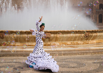 Flamenco dancer woman, teenage brunette and beautiful typical Spanish dancer is dancing between soap bubbles in front of a fountain. Flamenco concept of the cultural heritage of humanity