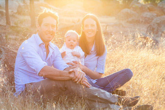 Young Family Seated In Dry Grass With Sun Flare