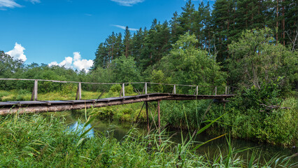 Landscape with forest river and old wooden bridge across the it.