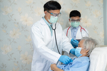 Asian doctor team check old senior lady patient for disease to motivation new normal to treat infection Covid19 Coronavirus at hospital ward.