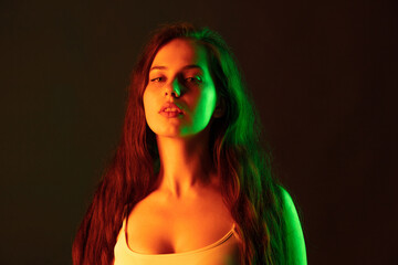 Portrait of beautiful young woman looking at camera, posing isolated over brown studio background in neon light