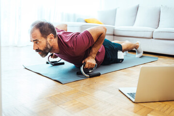 Mature adult man during fitness gymnastics online course workout at home looking at laptop stay at...