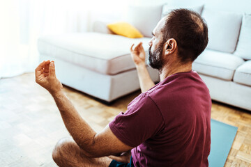 Fototapeta Calm healthy serene old middle aged mature man meditating with eyes closed sitting in yoga pose in living room at home. Breathing exercises, meditation, no stress, peace of mind, zen concept. obraz