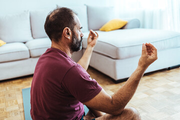 Fototapeta Mature man in sport clothing meditating while sitting on the floor in the lotus position at home. Mid adult man in morning meditation. obraz