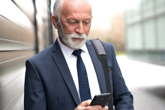 Senior businessman using phone in front of corporate office building