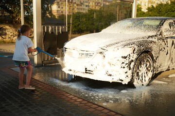 Family cleaning car in self-service at car wash during sunset. Car covered in white foam. Concept of easy and fun self-service