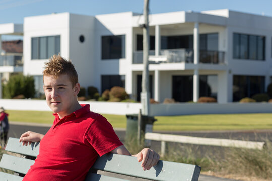 Ordinary teenage boy sitting on bench in front of mansion