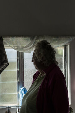 Elderly lady in gloomy room, looking out the window