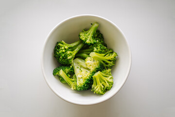 A bowl of cooked green broccoli, shot from above on a light background. Boiled broccoli vegetable...