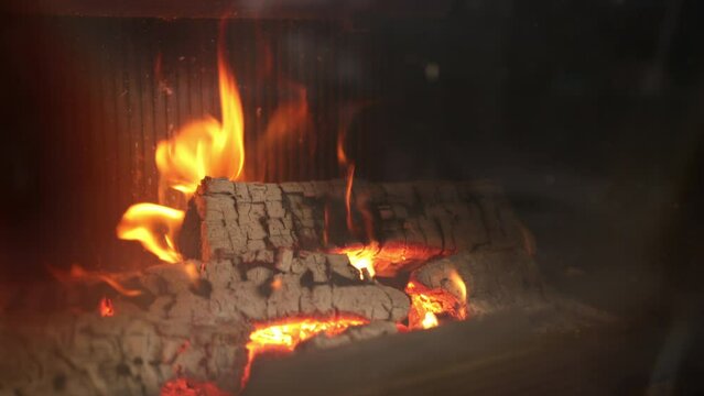 Concept of fireplace with fire at home. Comfortable living room log wood on top metal fireside, behind glass door. Burning firewood in fire-box hearth country cottage. Close up