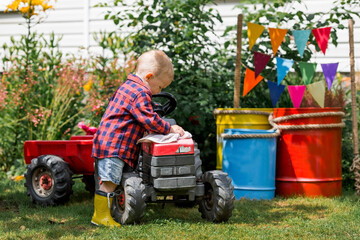 A cheerful boy dressed in a rustic style washes a tractor with a rag in the garden in the village....