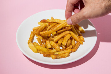 The hand takes french fries on a pink background. A delicious way to cook potatoes. Delicious fast food