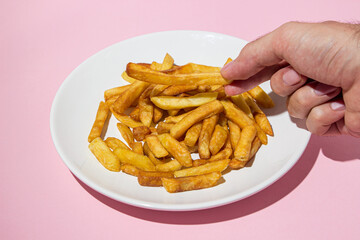 The hand takes french fries on a pink background. A delicious way to cook potatoes. Delicious fast food