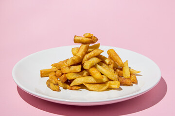 French fries on a white plate on a pink background. A delicious way to cook potatoes. Delicious fast food