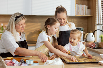 Older daughter and little one putting cookies on baking tray helping mother and granny baking cooking biscuits cookies cakes pie homemade pizza braed.