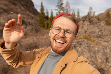 Concept Adventure Traveler with backpack. Hipster man in glasses and red hat takes selfie photo background autumn mountains Altai